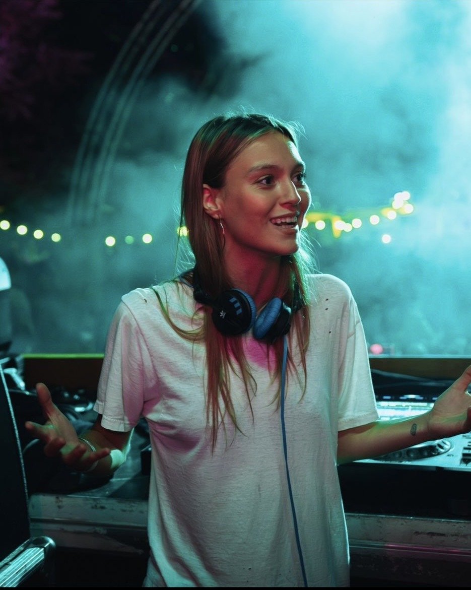 Paloma Le Friant sorrindo com camiseta branca e fones no pescoco