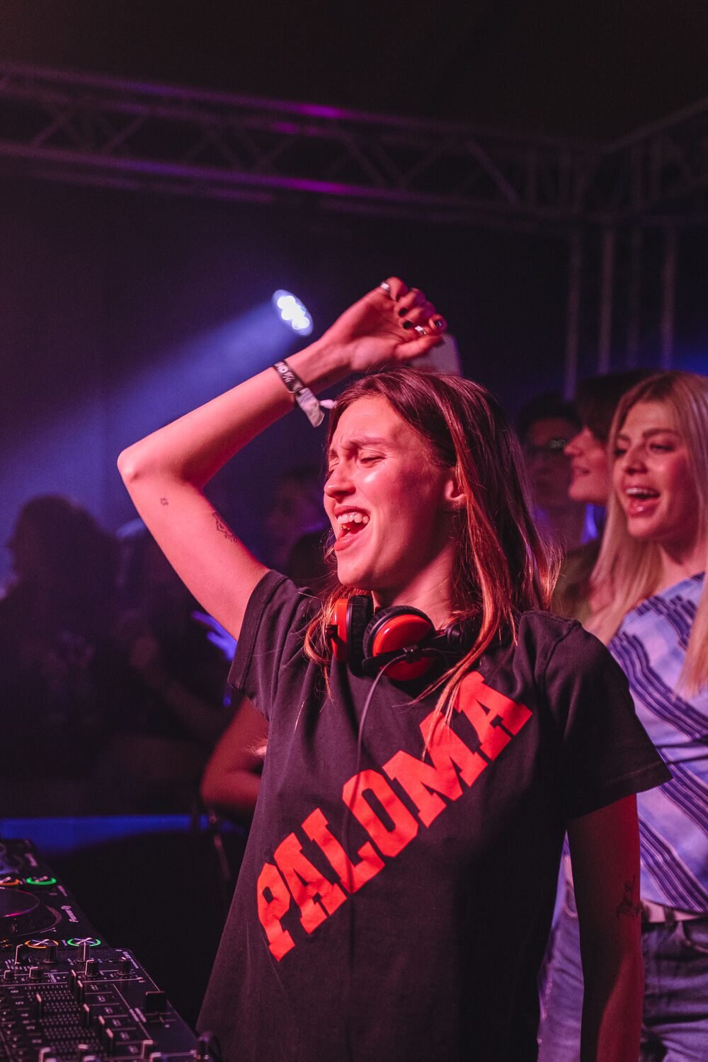 Paloma Le Friant discotecando com camiseta PALOMA sob luzes roxas