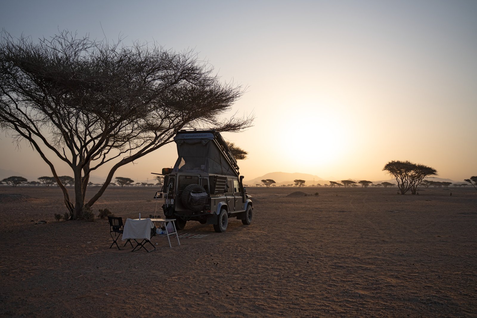 Land Rover Defender 110 em pôr do sol e poeira durante acampamento