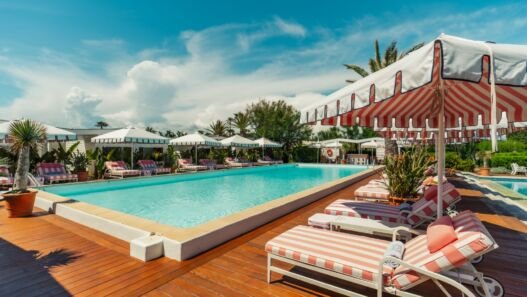 Piscina de 21 metros do Épi 1959 com deck de madeira, espreguiçadeiras listradas e guarda-sóis, na Baía de Pampelonne