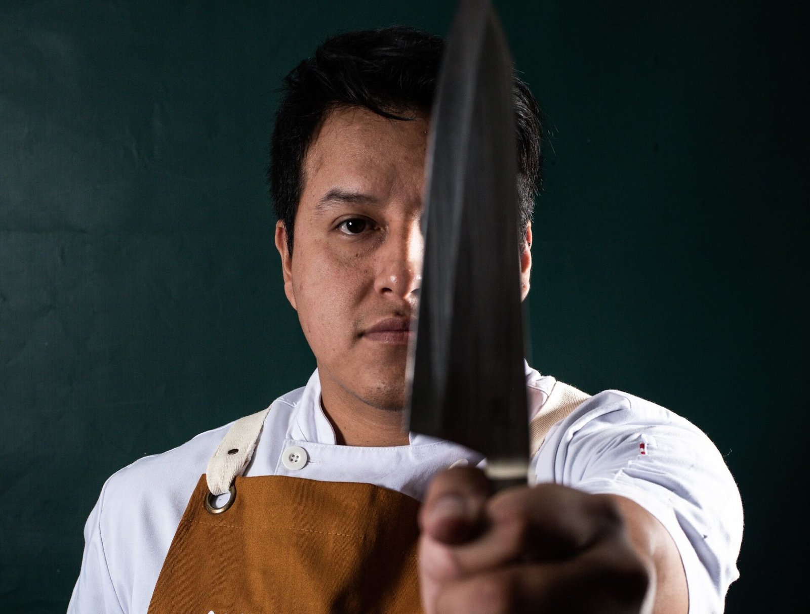 Retrato do chef Enrique Paredes segurando uma faca, em fundo escuro