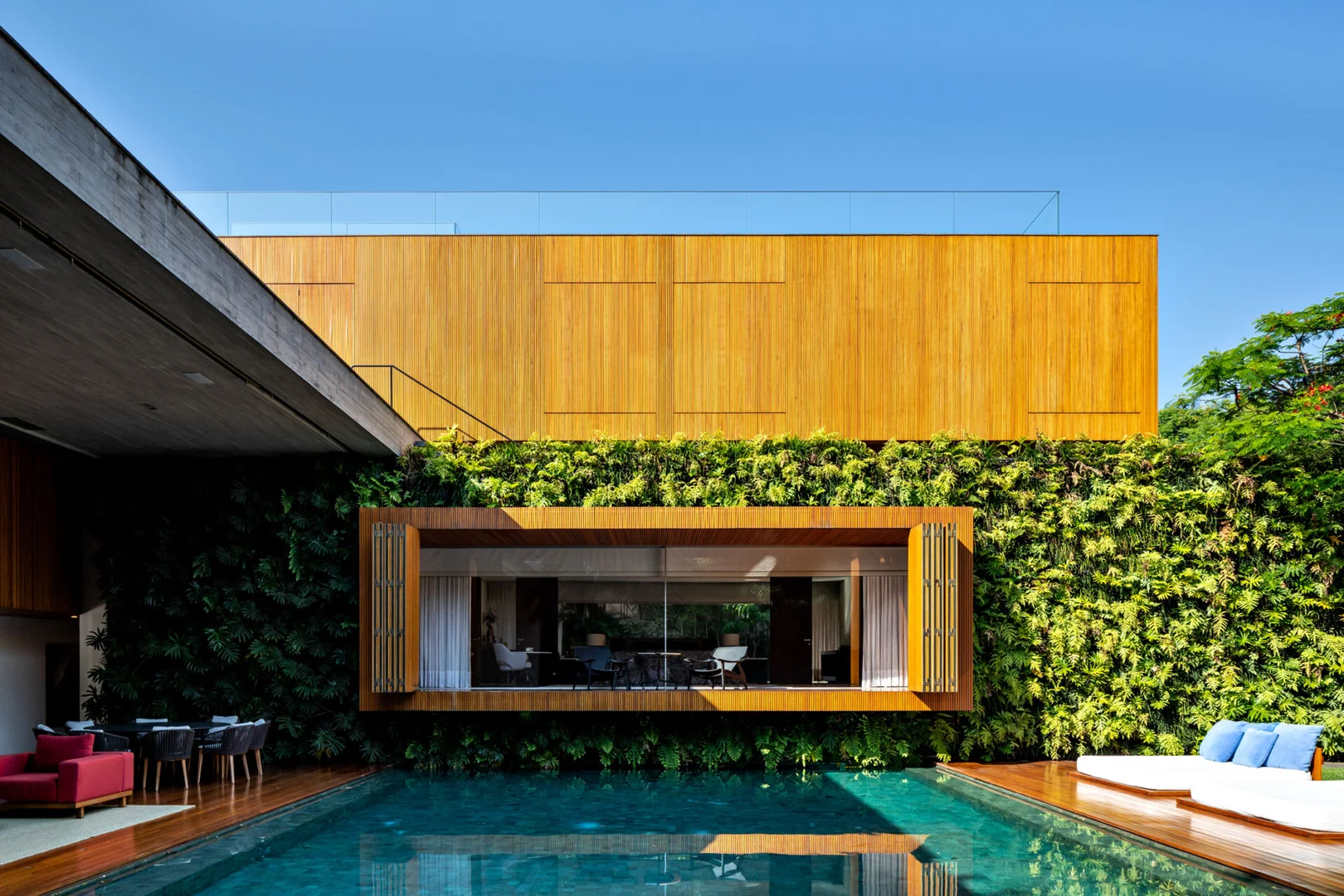 Volume revestido de madeira suspenso sobre a piscina, com jardim vertical ao fundo