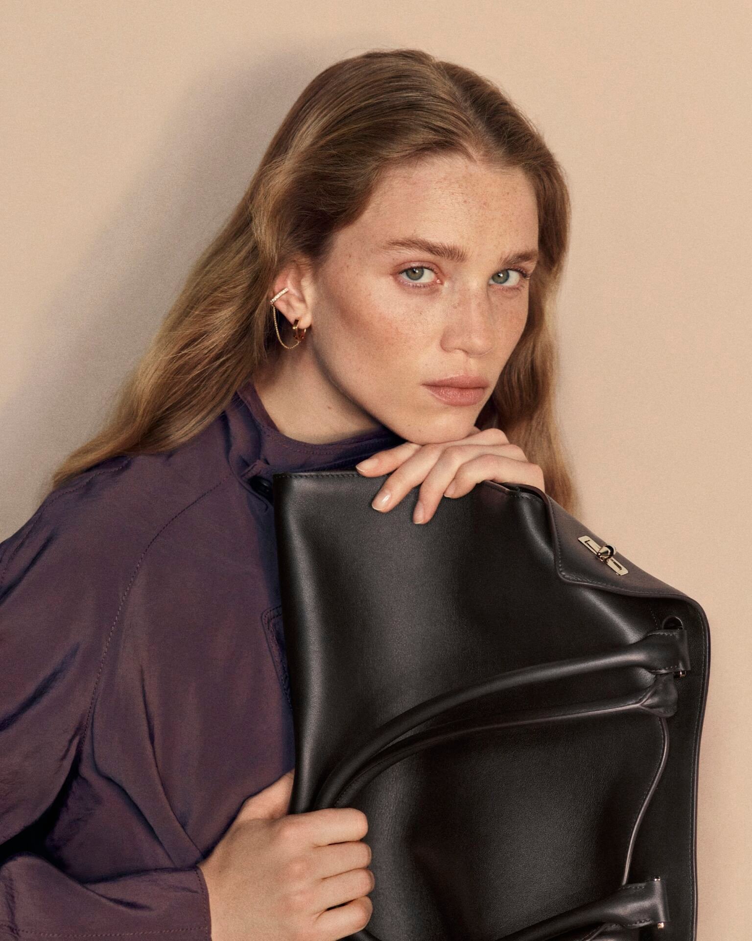 Modelo segura a bolsa Clash de Cartier preta junto ao rosto