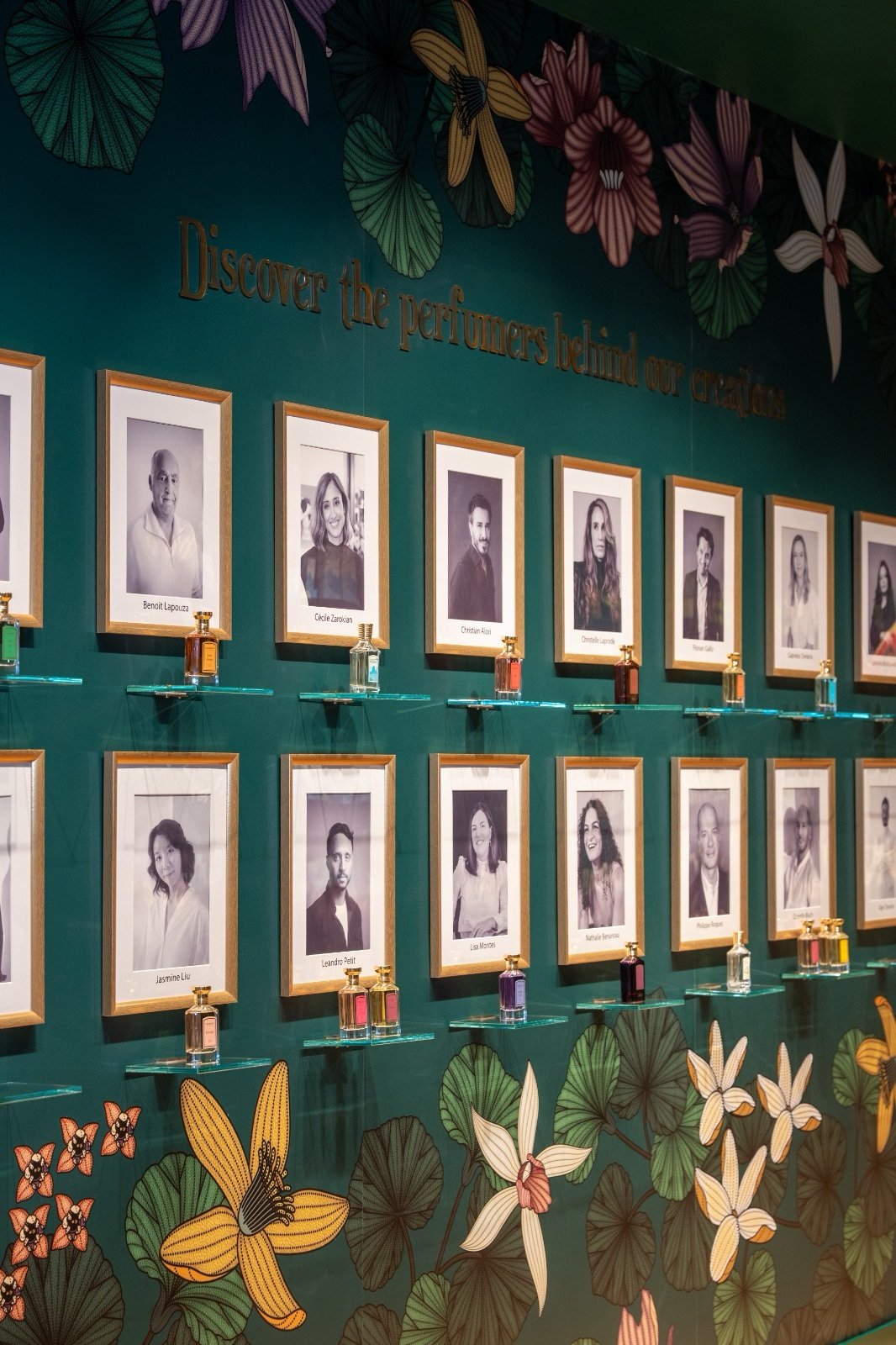 Parede com retratos e documentos emoldurados da história da Granado, sobre painel verde com flores ilustradas