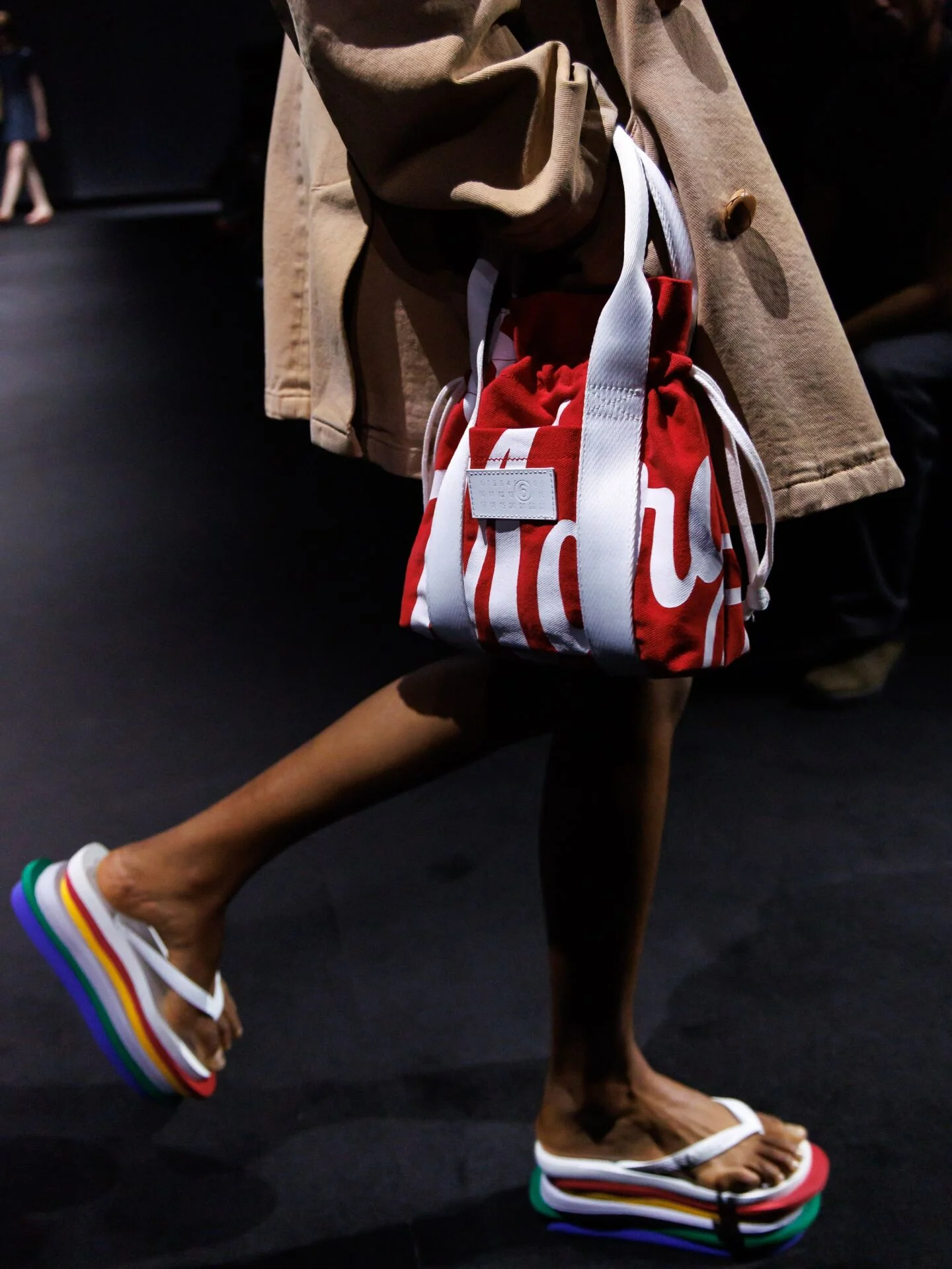 Detalhe da Top 6Layers em movimento na passarela, com bolsa vermelha ao lado