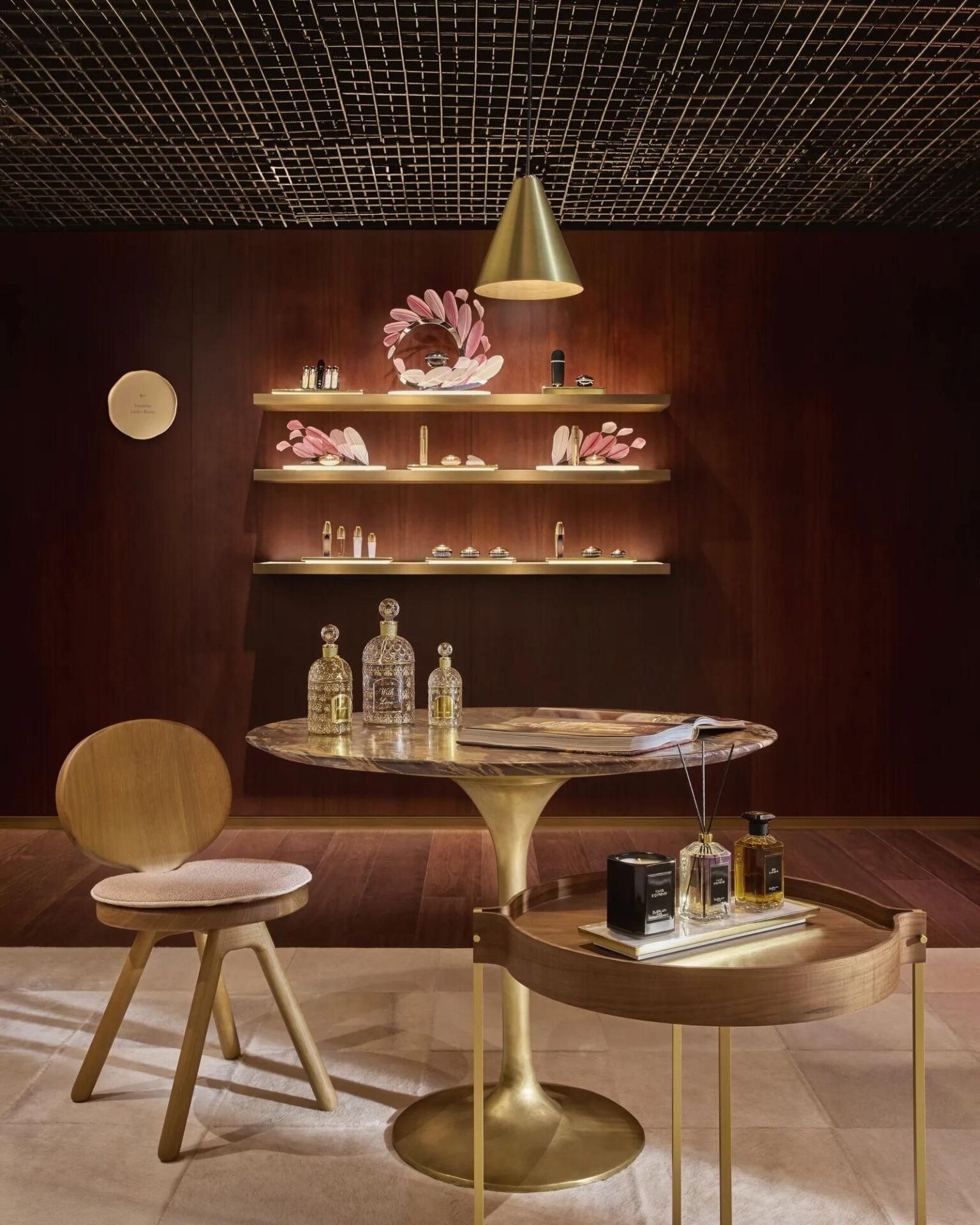 Recepção do Asaya Spa com frascos Guerlain em prateleiras de latão sobre parede de madeira e mesa redonda de mármore