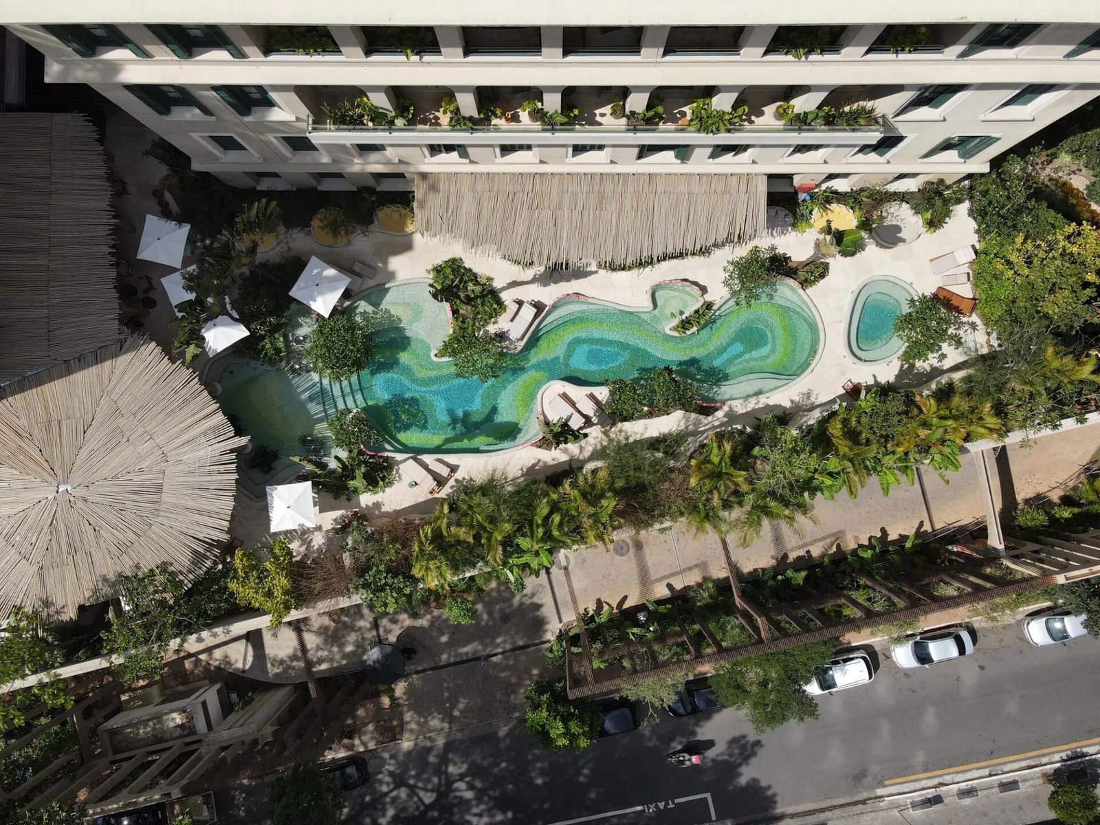Vista aérea da Emerald Pool, piscina de contornos orgânicos em tons de verde cercada por jardins, com a cobertura de madeira do complexo ao lado