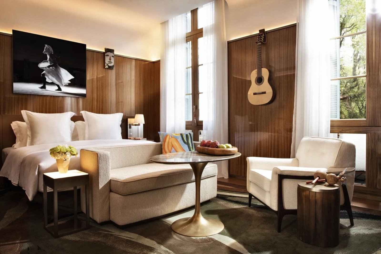 Grand Premier Room com cama de linho branco, violão pendurado na parede de madeira e fotografia em preto e branco sobre a cabeceira