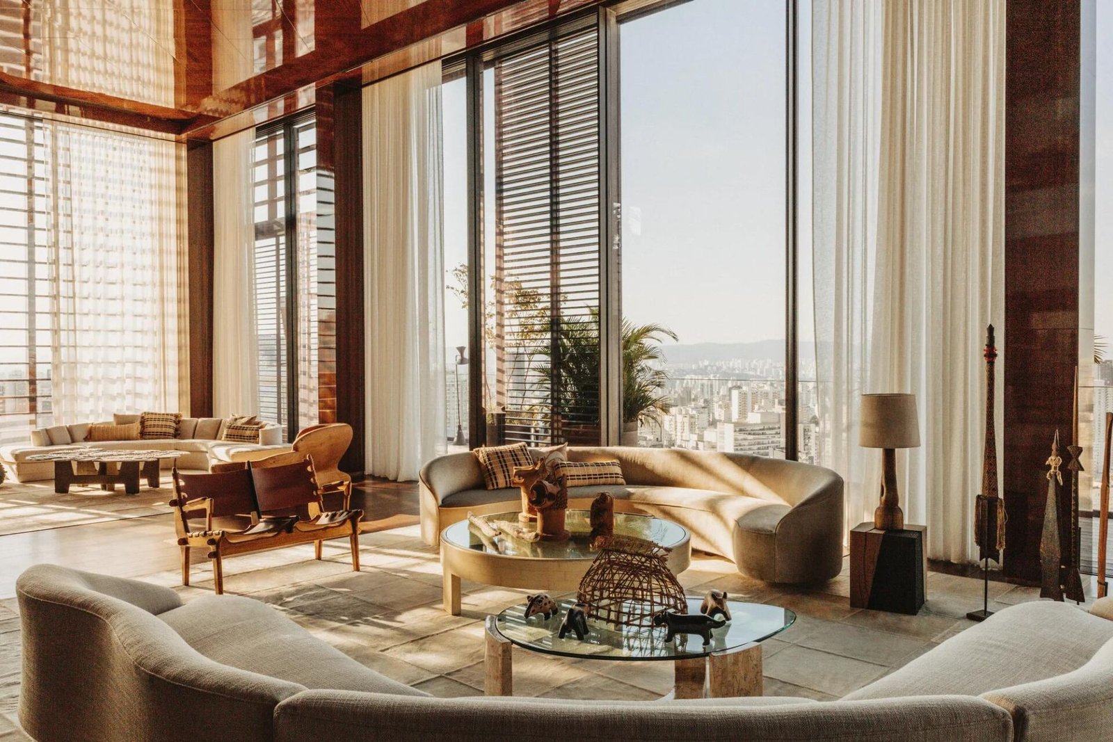 Sala da Penthouse com pé-direito duplo, sofás curvos, cortinas claras e janelas do piso ao teto com vista para o skyline de São Paulo