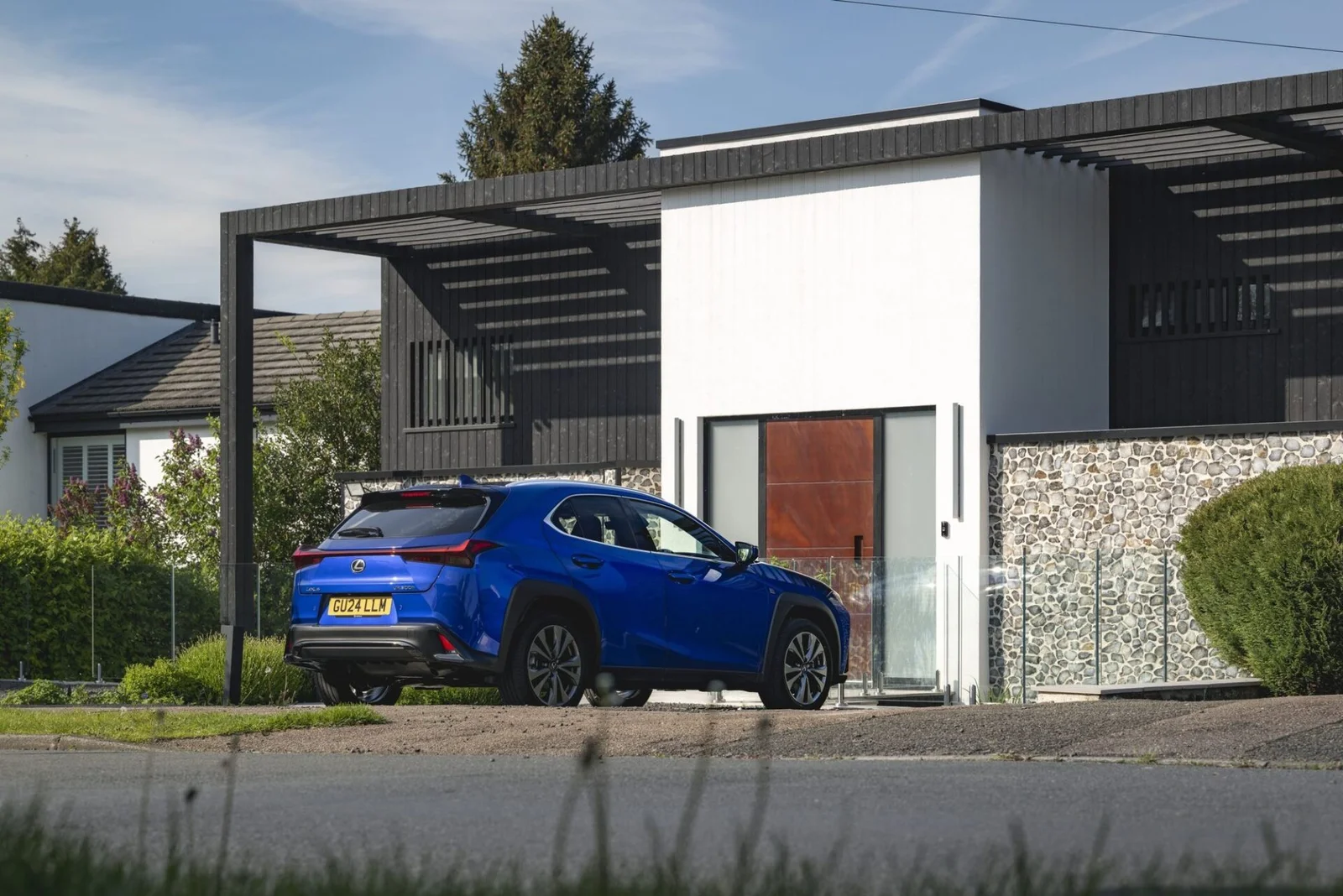 Lexus UX 300h estacionado em frente à entrada de uma casa contemporânea, visto de trás.