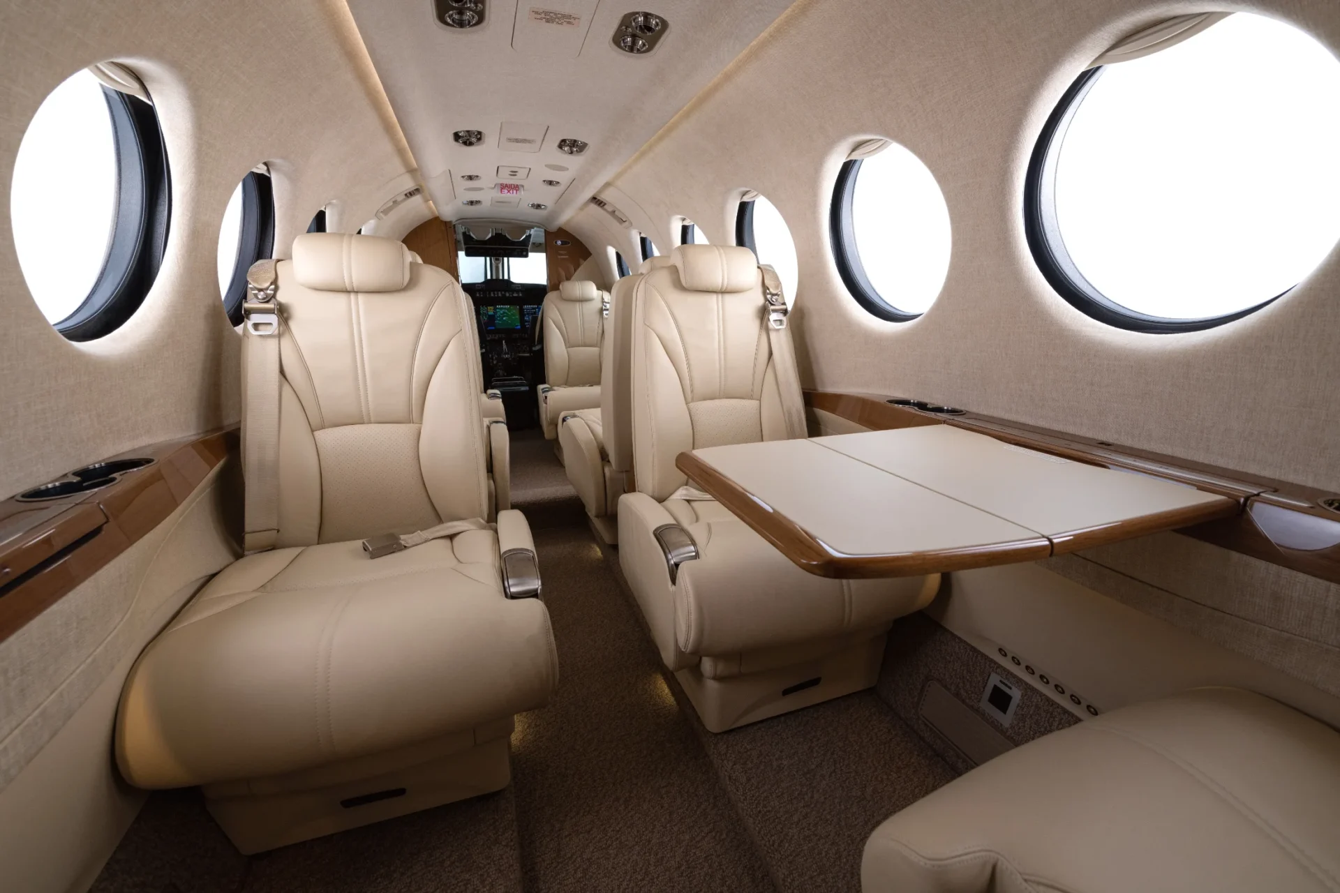 Cabine do Beechcraft King Air 360 em couro claro, com quatro poltronas em configuração club e mesas abertas