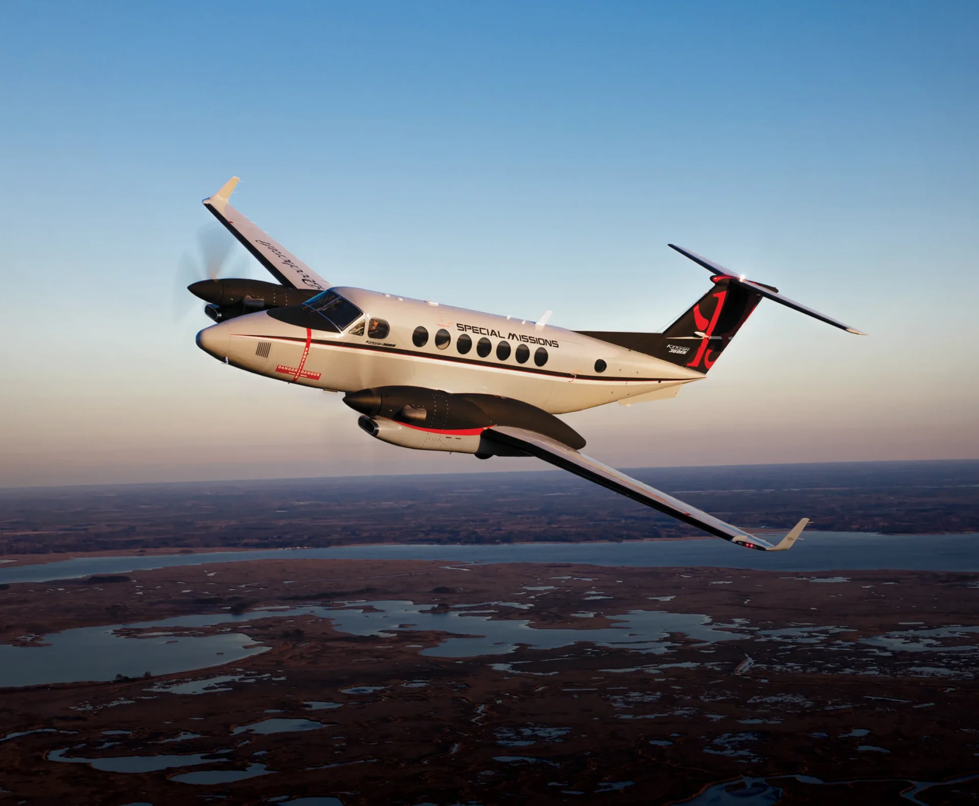 Beechcraft King Air 360ER em voo ao entardecer sobre área alagada