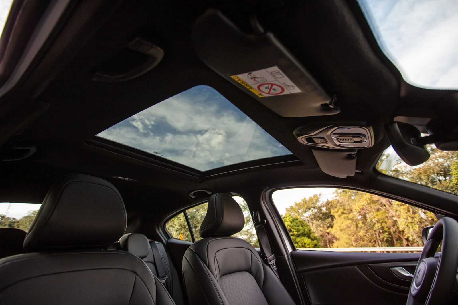 Vista interna do teto solar panorâmico do Fiat Fastback Impetus, com céu e nuvens acima dos bancos dianteiros em couro.